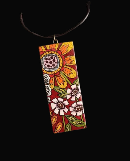 A hand-painted wooden necklace with vibrant colors and floral patterns, displayed against a dark background.